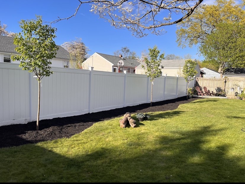 New white vinyl privacy fence with fresh mulch bed and young trees