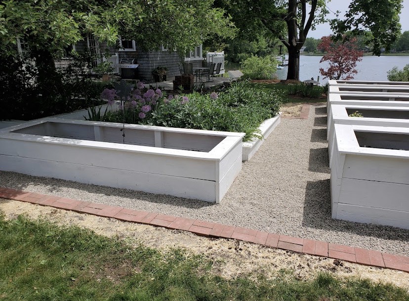 White raised garden beds with gravel walkways beside a lake